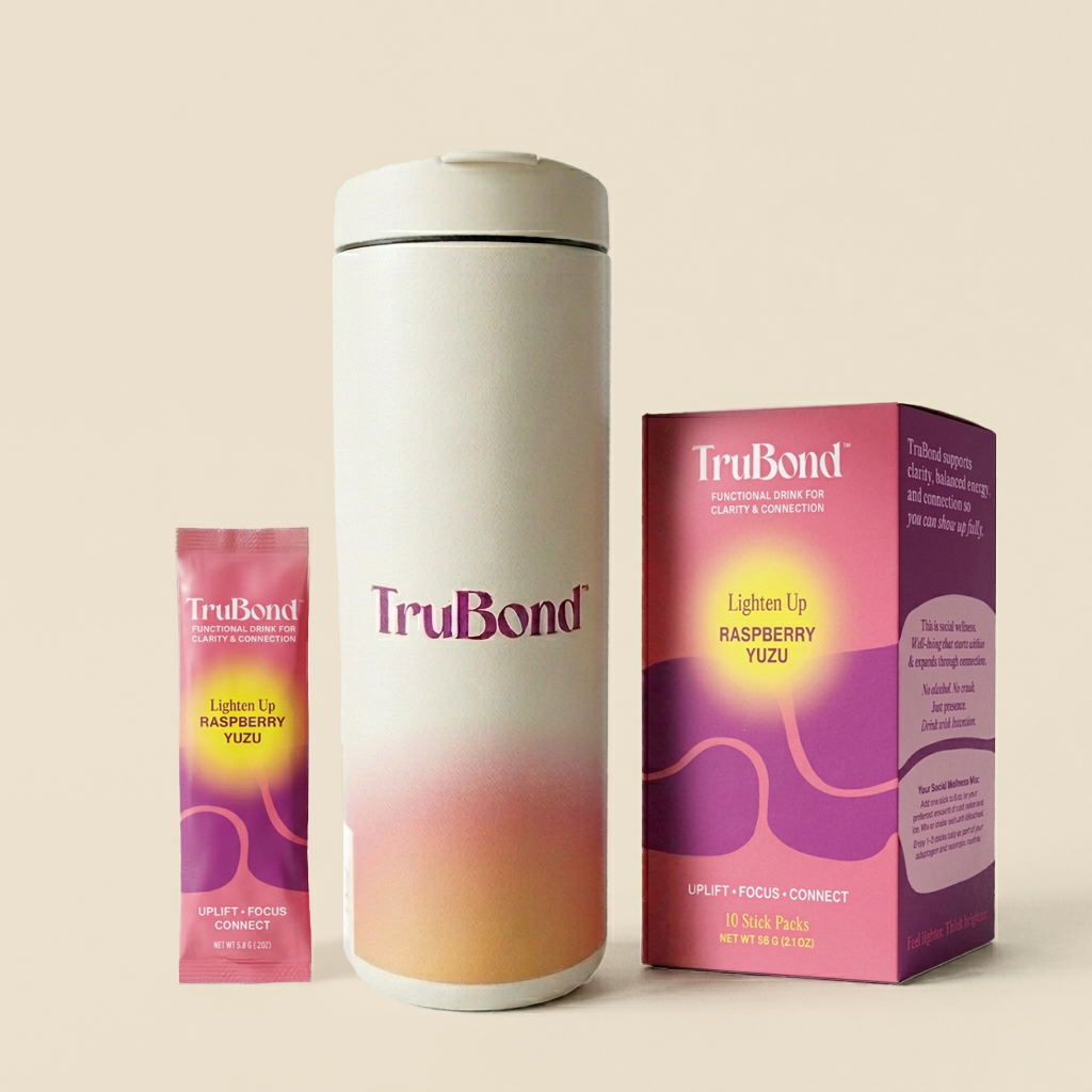 TruBond Lighten product packaging including a tall Miir Flip Traveler white tumbler, a small pink Lighten Up stick pack, and a Lighten Up box on a beige background.